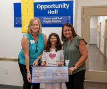 An 11-year-old girl stands with two other women holding a donation check