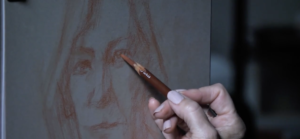 Artist drawing a woman's portrait using a red charcoal pencil