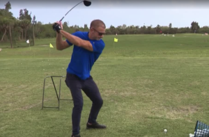 Man in a blue shirt golfing in mid-swing